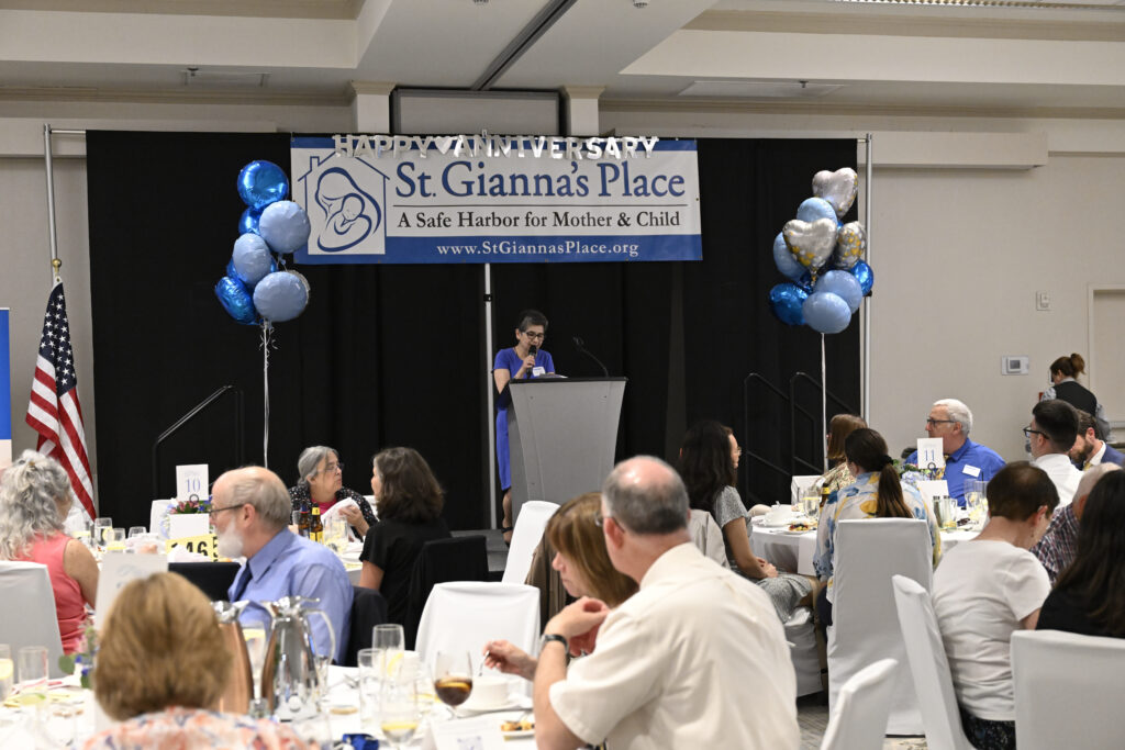 A woman speaking at a podium to a room full of people sitting at tables